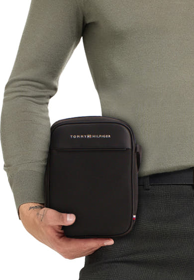 Zwarte schoudertas van TOMMY JEANS, gedragen door een man in een groene trui en geruite broek.