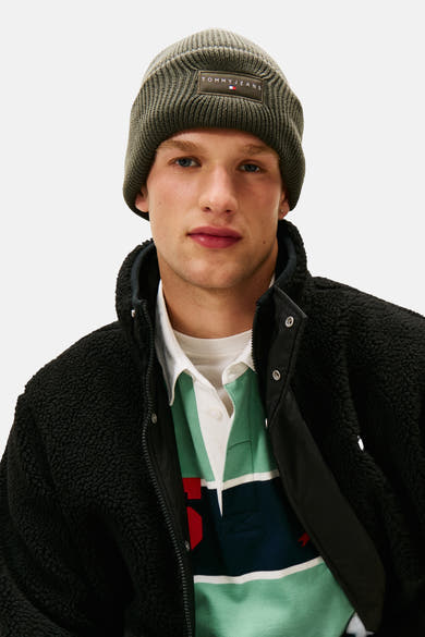 Kaki muts van Tommy Jeans, gedragen met een zwarte sherpa jas en een gestreept poloshirt.