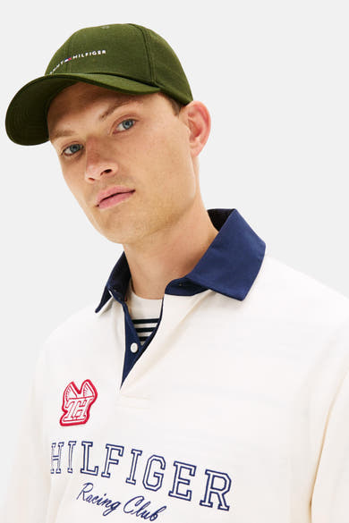 Casquette verte de TOMMY JEANS avec logo brodé et un homme portant un polo blanc cassé.
