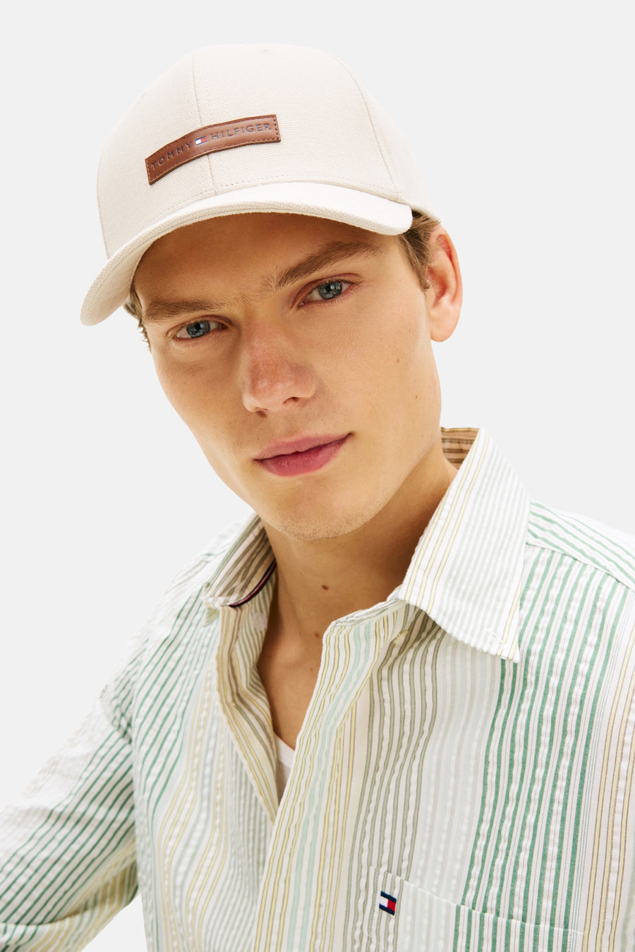 Casquette beige de Tommy Jeans avec logo rectangulaire sur le devant, portée avec une chemise rayée.