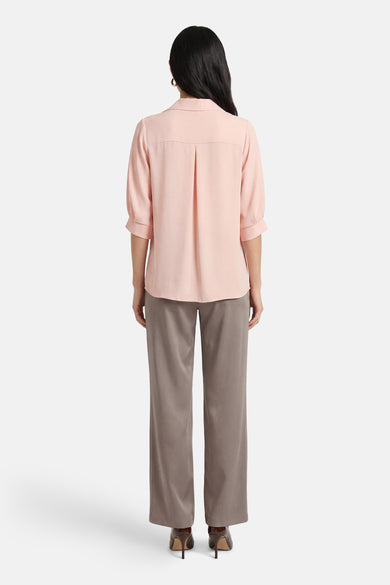 Chemisier rose à manches courtes par AMELIE ET AMELIE, avec plis au dos et porté avec un pantalon gris.