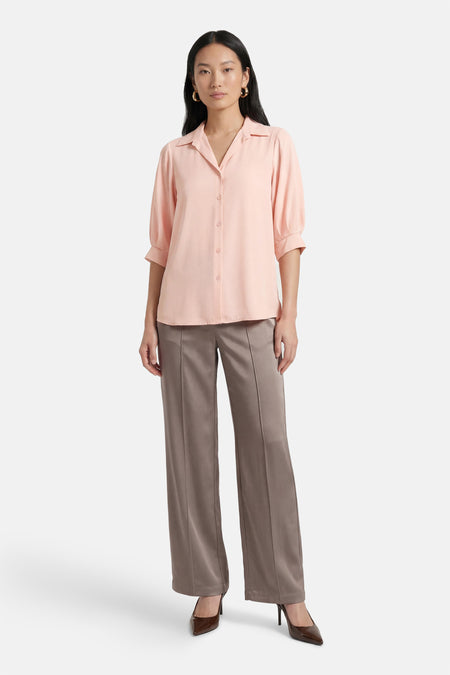 Chemisier rose à manches courtes par AMELIE ET AMELIE, porté avec un pantalon et des escarpins marron.