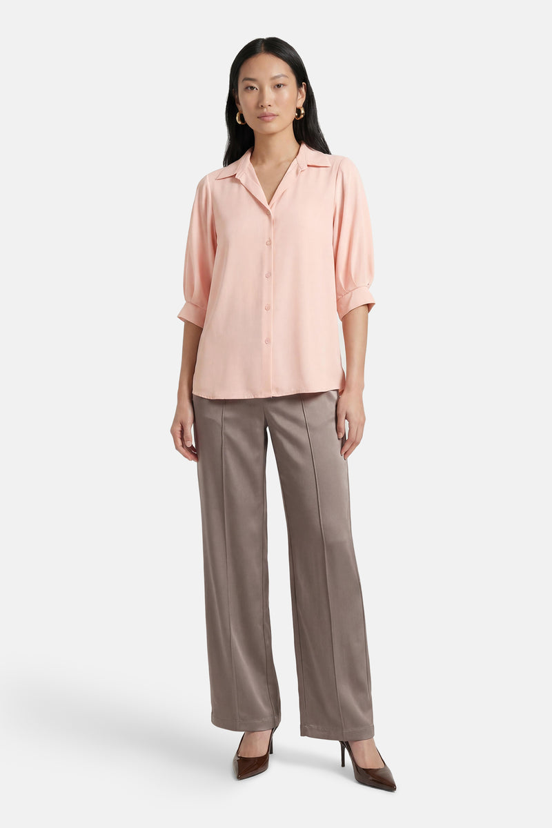 Chemisier rose à manches courtes par AMELIE ET AMELIE, porté avec un pantalon et des escarpins marron.