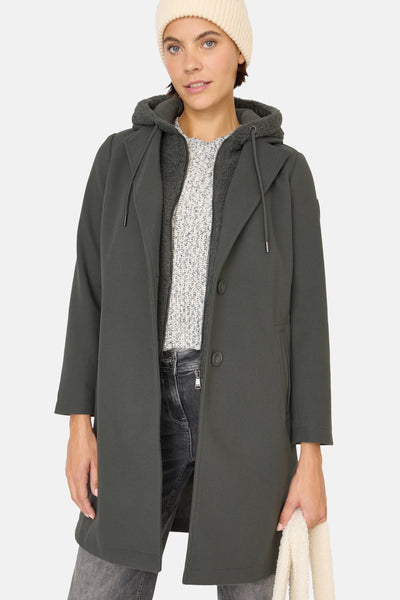 Veste longue verte de CECIL, à capuche doublée en peau de mouton, portée sur un pull en tricot.