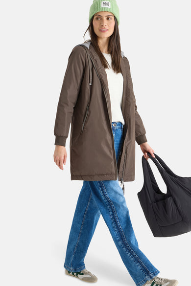 Veste longue marron de CECIL, avec une capuche grise, portée avec un jean bleu et un bonnet vert.
