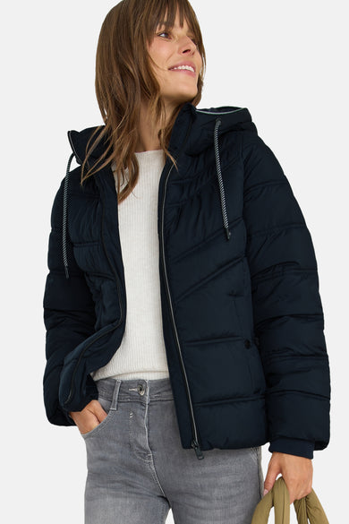 Korte blauwe jas van CECIL met capuchon en koorden, gedragen met een witte trui en een grijze jeans.