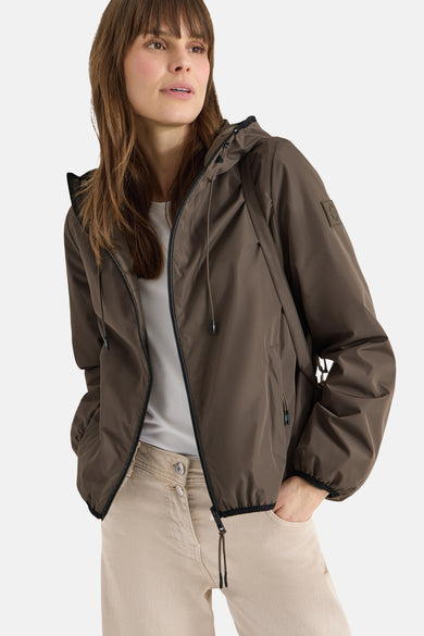 Veste courte brune de CECIL, avec capuche à cordon, portée sur un t-shirt blanc et un pantalon beige.