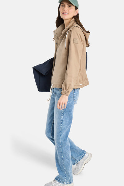 Veste courte beige de CECIL, avec capuche et cordon coulissant blanc, portée avec un jean bleu et des baskets argentées.