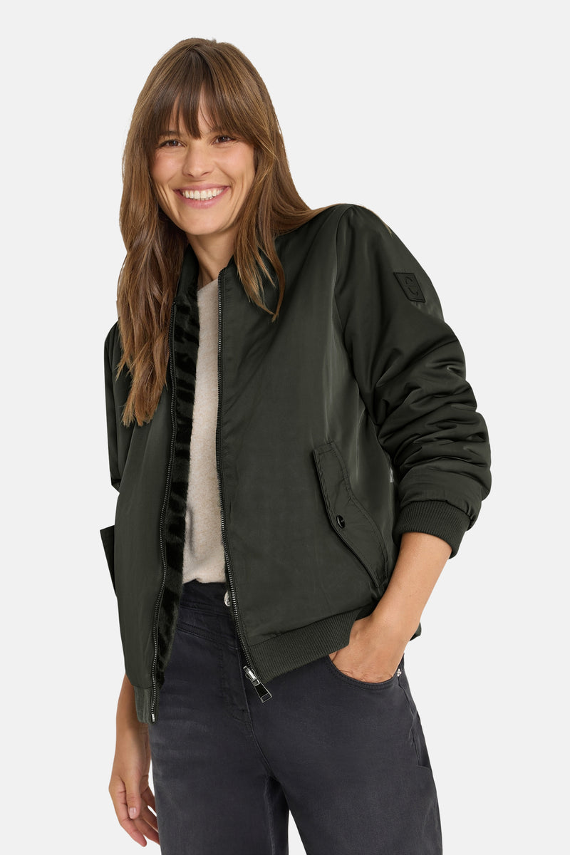 Kort groen jasje van CECIL, met ritssluiting en knoopzakken, gedragen met een zwarte jeans.