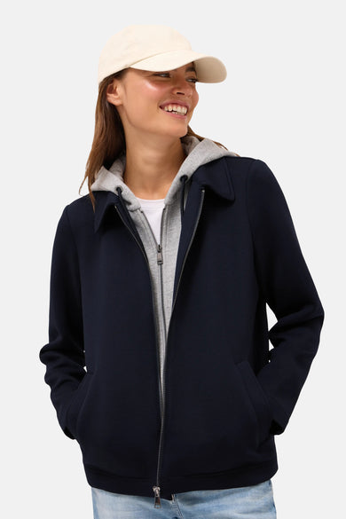 Kort marineblauw jack van CECIL, met grijze capuchon met rits en zakken, gedragen met een beige pet.