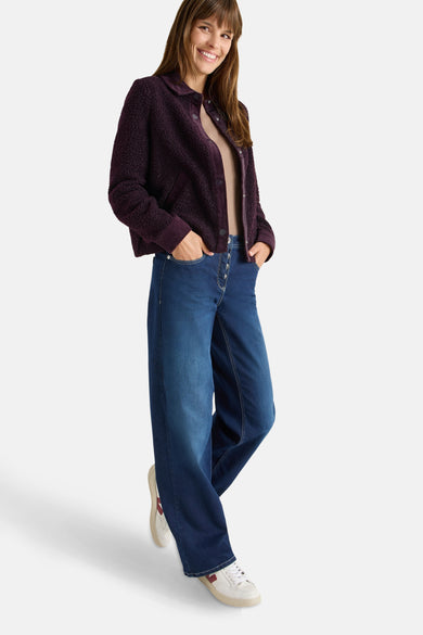 Veste courte mauve de CECIL, avec une texture bouclée, portée avec un jean large et des baskets blanches.
