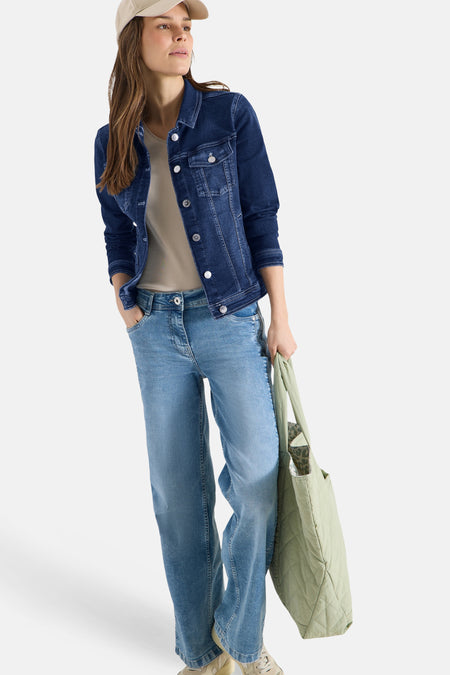 Veste en jean bleu moyen de CECIL, portée avec un t-shirt neutre, un jean ample et un sac vert.