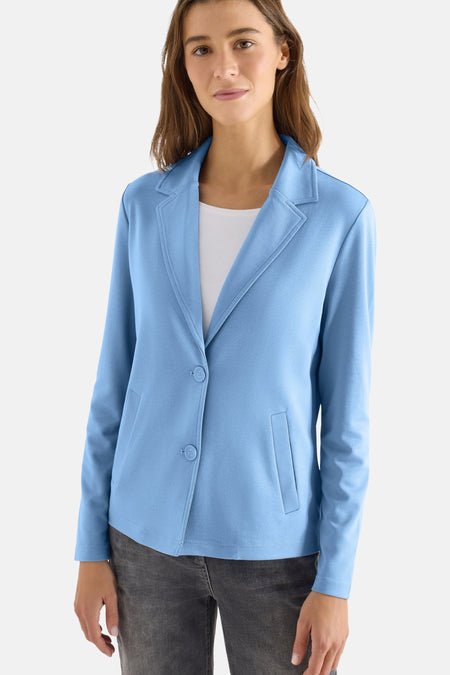 Blauwe blazer van CECIL, gedragen met een wit T-shirt en een donkergrijze jeans, op een houten stoel.