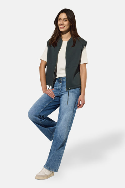 Groen vest van CECIL, met ritssluiting aan de voorkant, gedragen over een wit T-shirt en een wijde blauwe spijkerbroek met witte sneakers.