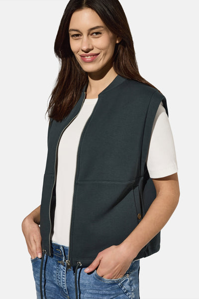Groen gilet van CECIL, met zilveren ritssluiting, gedragen over een wit T-shirt en een blauwe jeans.