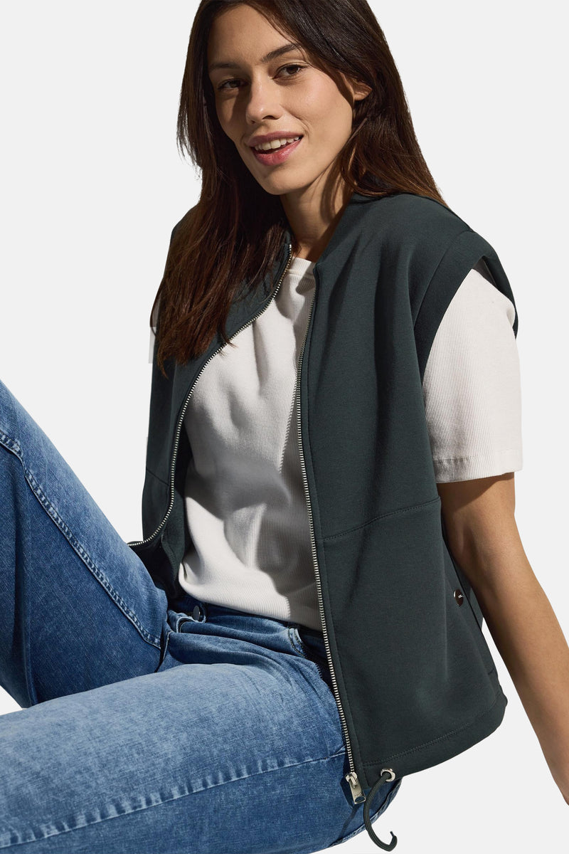 Groen vest van CECIL met zilveren ritssluiting gedragen over een wit T-shirt en een blauwe jeans.