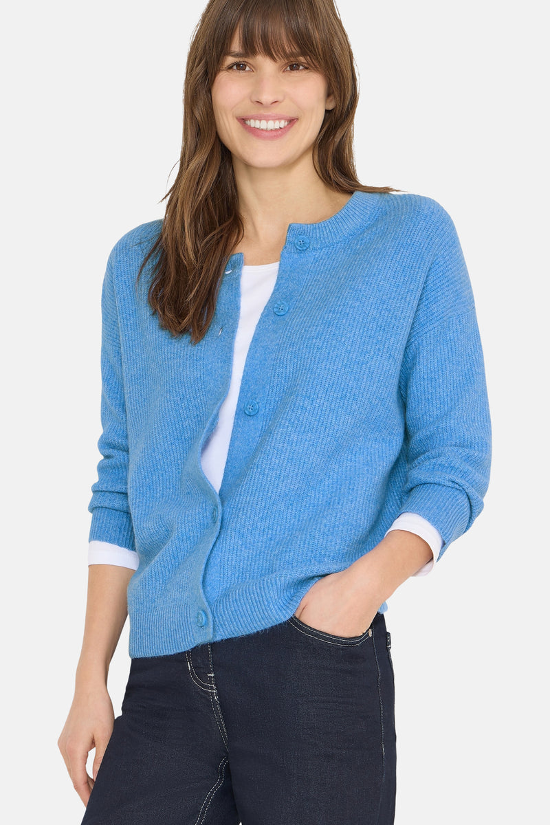 Cardigan bleu de CECIL, porté sur un t-shirt blanc, avec un jean foncé et une main dans la poche.
