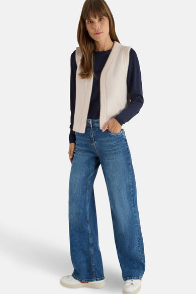 Gilet écru de CECIL porté avec un pull bleu marine et un jean bleu large.