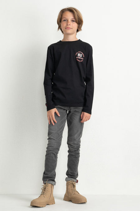 Black long-sleeve T-shirt with chest logo and sleeve text, worn by model in gray jeans and tan boots, full front view