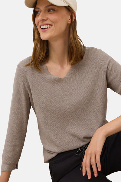 Pull à col en V brun de CECIL, en maille texturée, porté avec un pantalon noir et une casquette beige.
