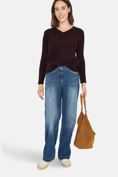 Pull col V rouge par CECIL, porté avec un jean bleu ample et un sac marron en daim.
