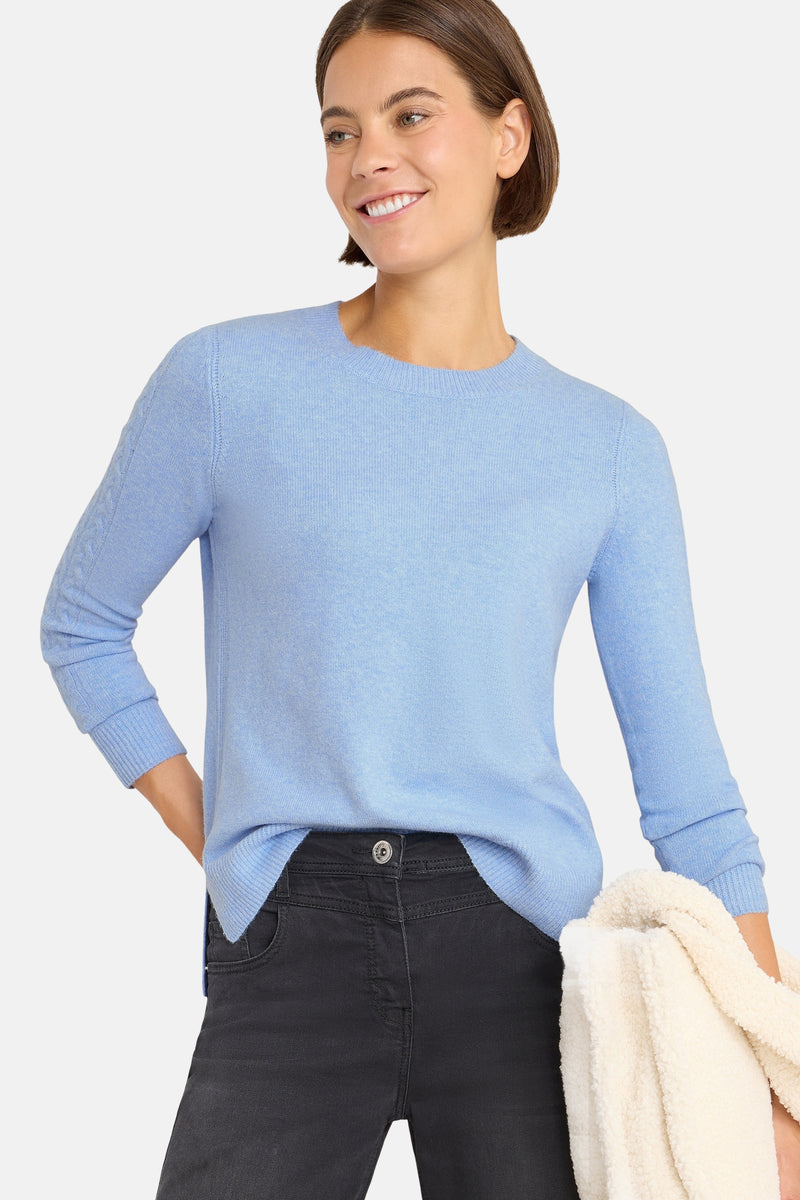 Pull à col rond bleu de CECIL, avec des manches longues à détails tressés et porté avec un pantalon noir.
