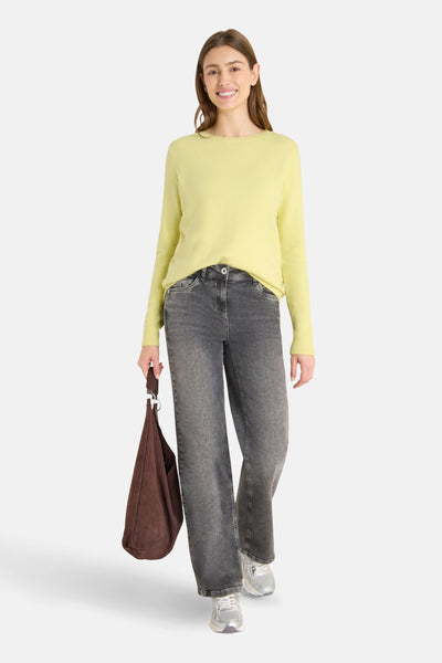 Pull à col rond jaune de CECIL, porté avec un jean gris délavé et des baskets argentées, tenant un sac marron.
