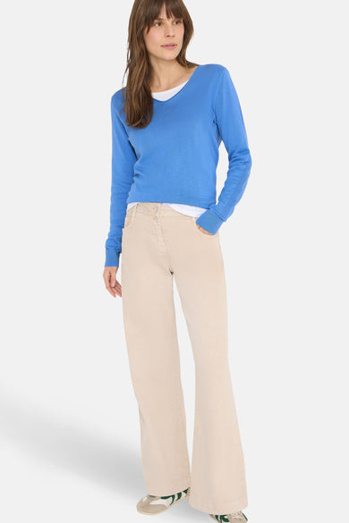 Pull à col en V bleu de CECIL, porté avec un jean beige à jambes évasées et des baskets.