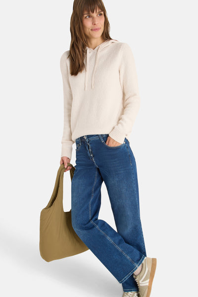 Pull à capuche écru de CECIL, porté avec un jean bleu et un sac fourre-tout olive.