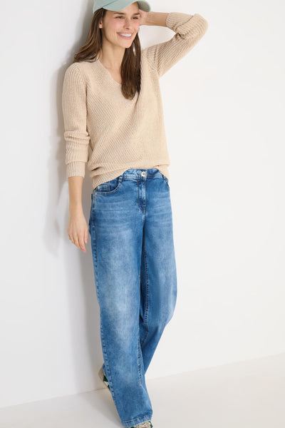 Pull col V beige de CECIL, porté avec un jean bleu décontracté et une casquette verte.