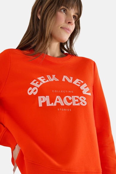 Oranje sweatshirt van CECIL met witte opdruk, gedragen met een beige broek en sneakers.
