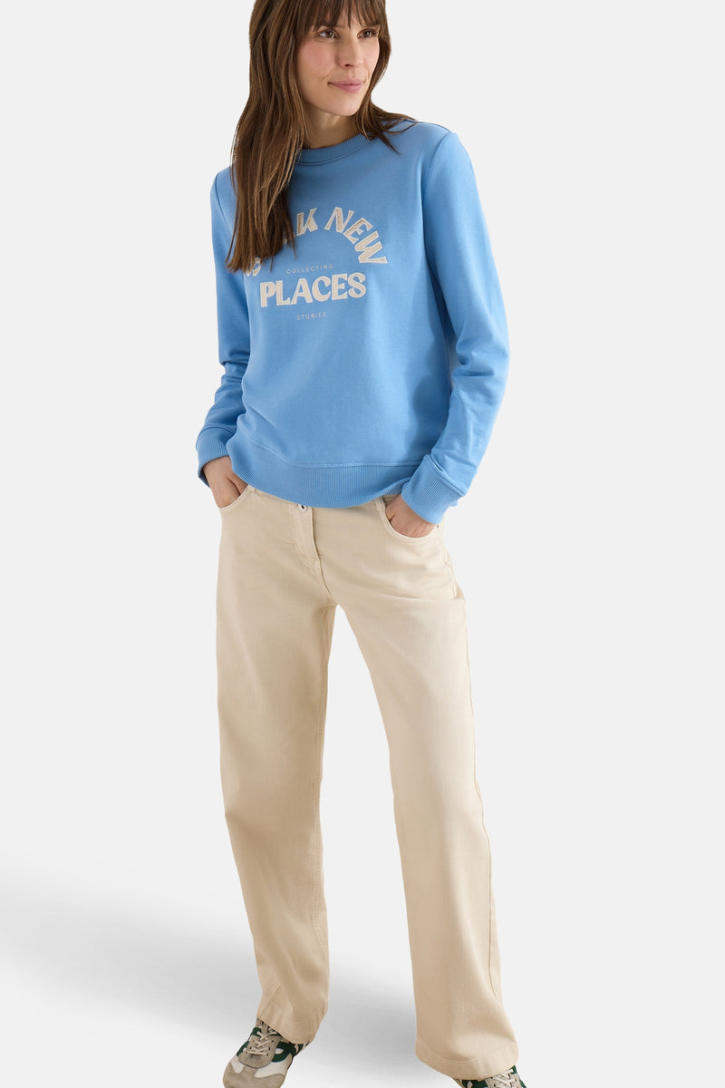 Blauwe trui van CECIL, met een decoratieve print op de voorkant, gedragen met een beige broek en sportschoenen.