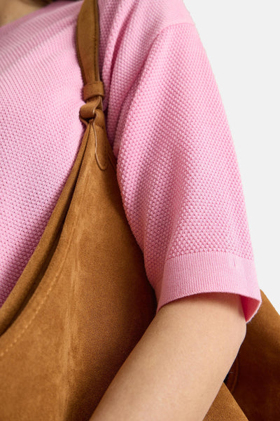 Pink textured short-sleeve pullover with ribbed cuff, worn with brown suede bag, side view close-up