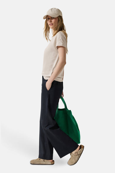 Top uni manches courtes beige de CECIL, avec boutons décoratifs sur les manches, porté avec un pantalon bleu marine et un sac vert.