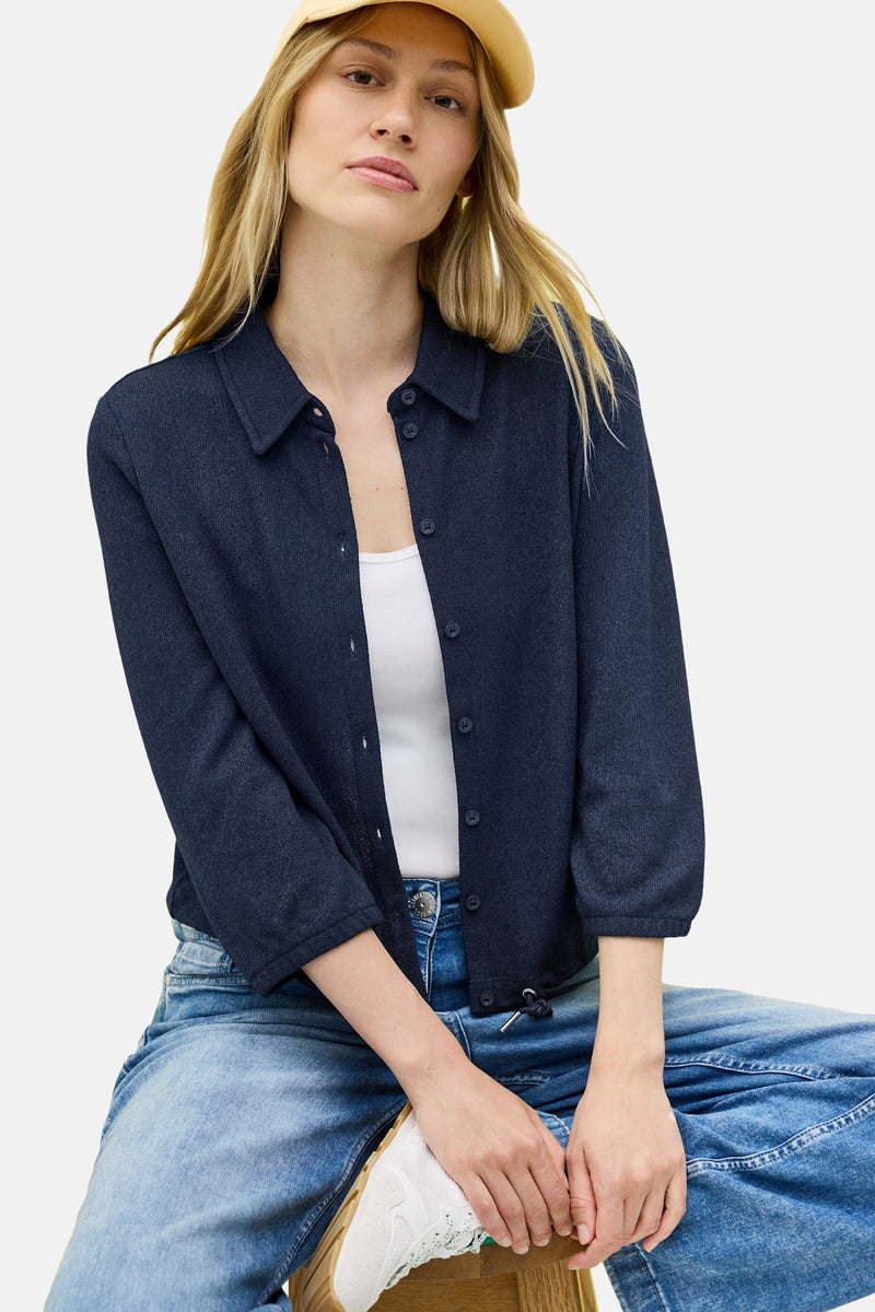 Blouse met lange mouwen blauw van CECIL, gedragen met een witte tanktop, wijde blauwe jeans en witte sneakers.