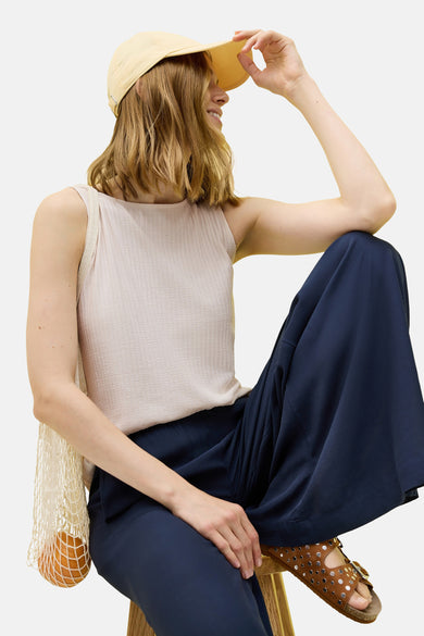 Beige mouwloze top van CECIL, geribbelde textuur, gedragen met een marineblauwe wijde broek en een gele pet.