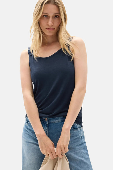 Mouwloos blauw topje van CECIL, gedragen met een lichtblauwe jeans, met een beige tas in de hand.