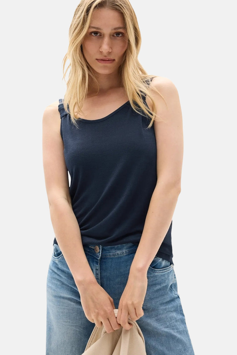 Mouwloos blauw topje van CECIL, gedragen met een lichtblauwe jeans, met een beige tas in de hand.