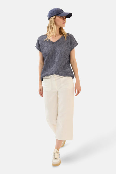 Blauwe blouse met korte mouwen van CECIL, met een getextureerd patroon, gedragen met een witte broek en een pet.