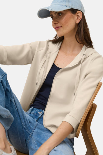 Beige vest van CECIL met ritssluiting, capuchon met trekkoord en gedragen over een marineblauwe tanktop.
