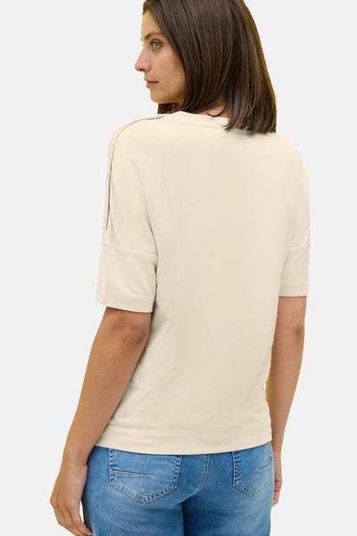 Beige T-shirt met korte mouwen van CECIL, opgerolde mouwen en decoratieve naden op de schouders, gedragen met een blauwe jeans.