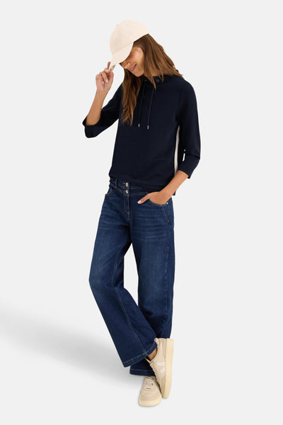 Sweat à capuche bleu marine de CECIL, avec des manches trois-quarts et porté avec un jean large et des baskets beiges.
