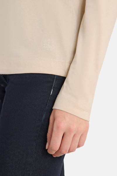 Beige blouse met lange mouwen van CECIL, met de tekst "BEYOND LIMITS", gedragen met een spijkerbroek.