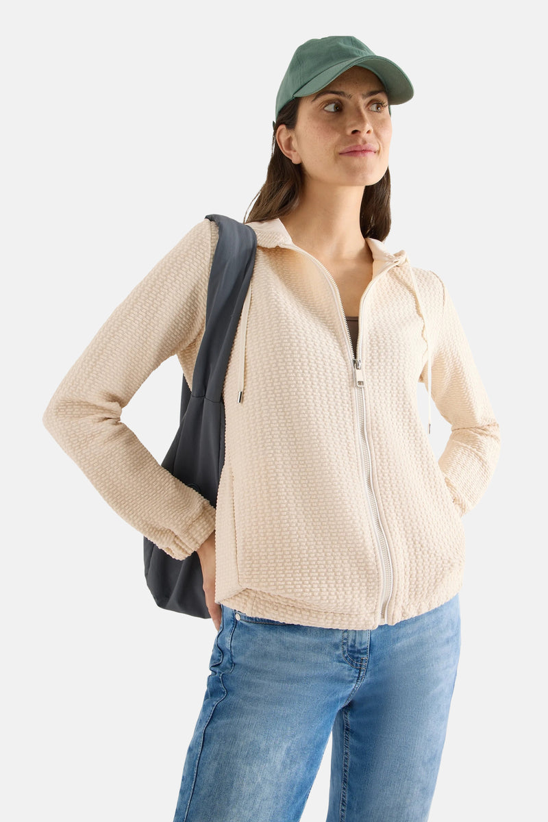 Gilet beige van CECIL, avec une texture gaufrée, porté avec un chapeau et un jean.