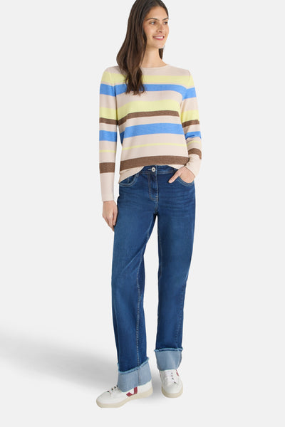 Pull à col rond multicolore de CECIL, avec rayures horizontales et porté avec un jean bleu et des baskets blanches.
