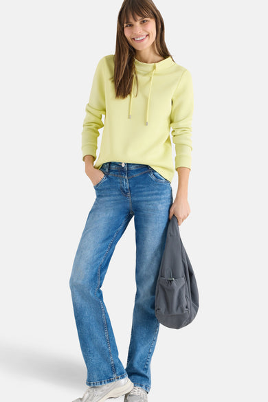 Sweat jaune de CECIL, avec capuche à cordon, porté avec un jean et des baskets argentées.