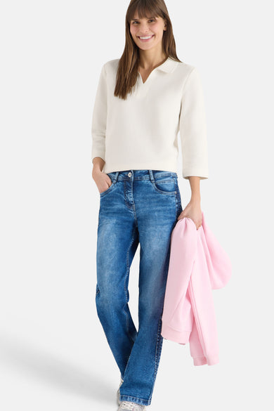 Polo blanc à manches longues de CECIL, porté avec un jean bleu et un gilet rose.