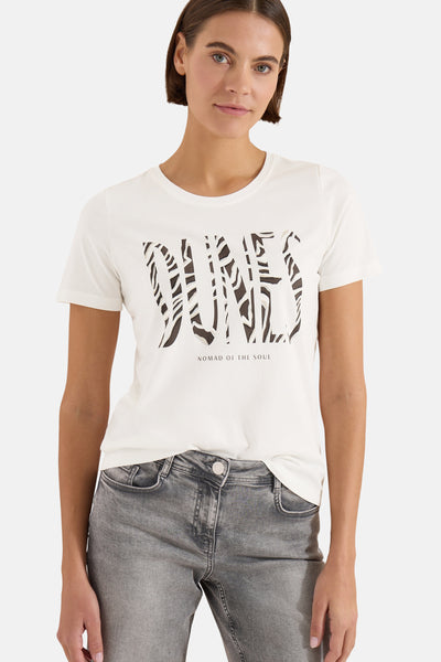 White short-sleeve t-shirt with bold zebra-print "DUNES" graphic and "NOMAD OF THE SOUL" text, worn by model with gray jeans, front view.