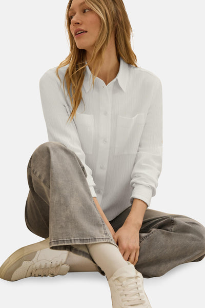 Chemise blanche à manches longues de CECIL, portée avec un pantalon gris et des baskets crème.
