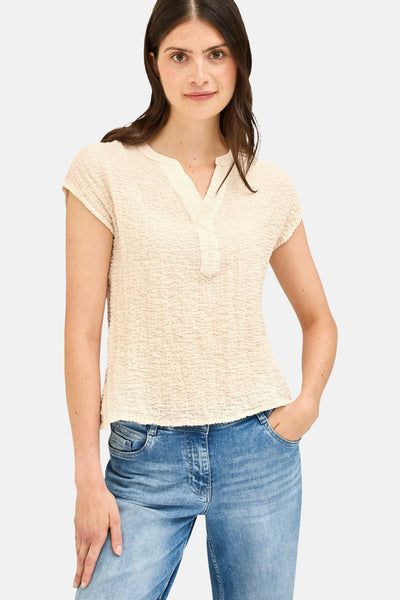 Blouse beige à manches courtes de CECIL, avec un col en V et une texture gaufrée, portée avec un jean.
